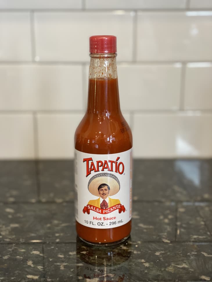 Tapatío hot sauce bottle on a dark granite countertop with a tiled backsplash.