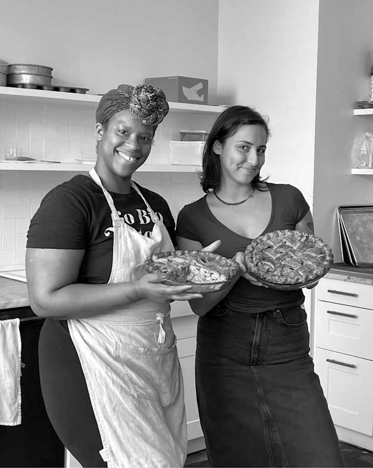 Two people in a kitchen holding pies and smiling.