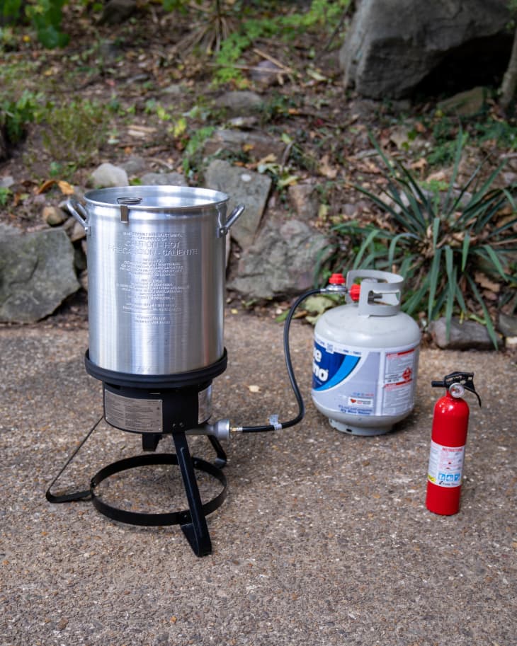 Outdoor deep-fryer setup with propane tank and fire extinguisher on a patio.