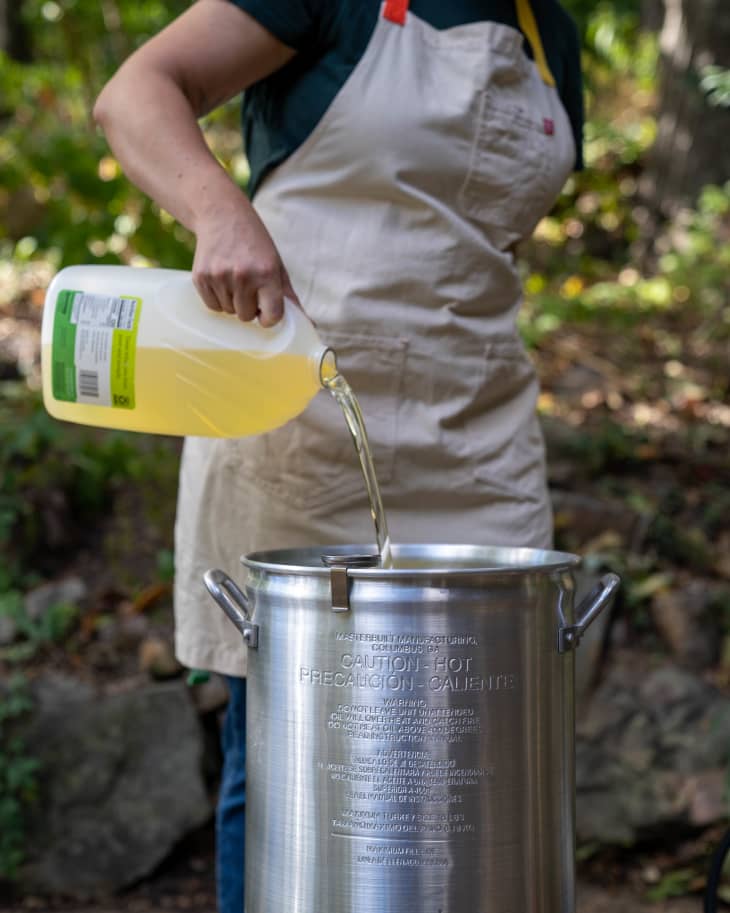 Pouring oil into a large metal pot outdoors, preparing for deep-frying turkey.