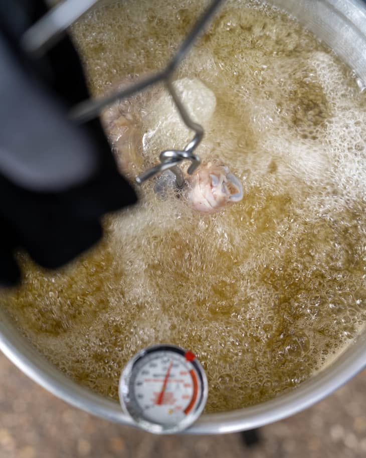 Turkey being deep-fried in hot oil with a thermometer in the pot.