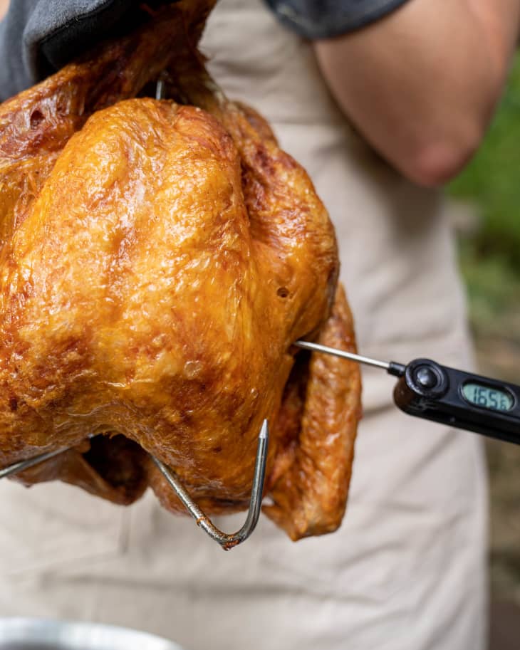 Golden deep-fried turkey being checked with a meat thermometer.