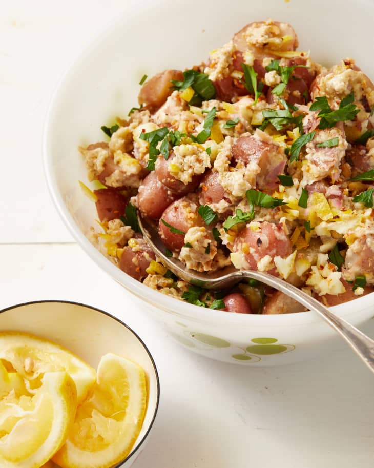 Potato salad with chopped parsley and lemon zest in a bowl, next to a dish of lemon wedges.