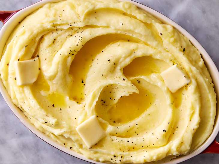 Creamy mashed potatoes in a red baking dish, topped with melted butter and black pepper