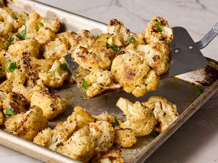Roasted cauliflower florets on a baking sheet, garnished with herbs and lightly charred.