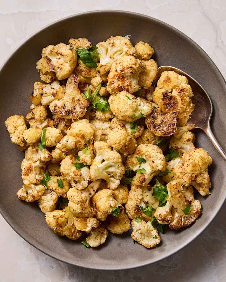 Roasted cauliflower florets garnished with fresh parsley in a gray bowl.