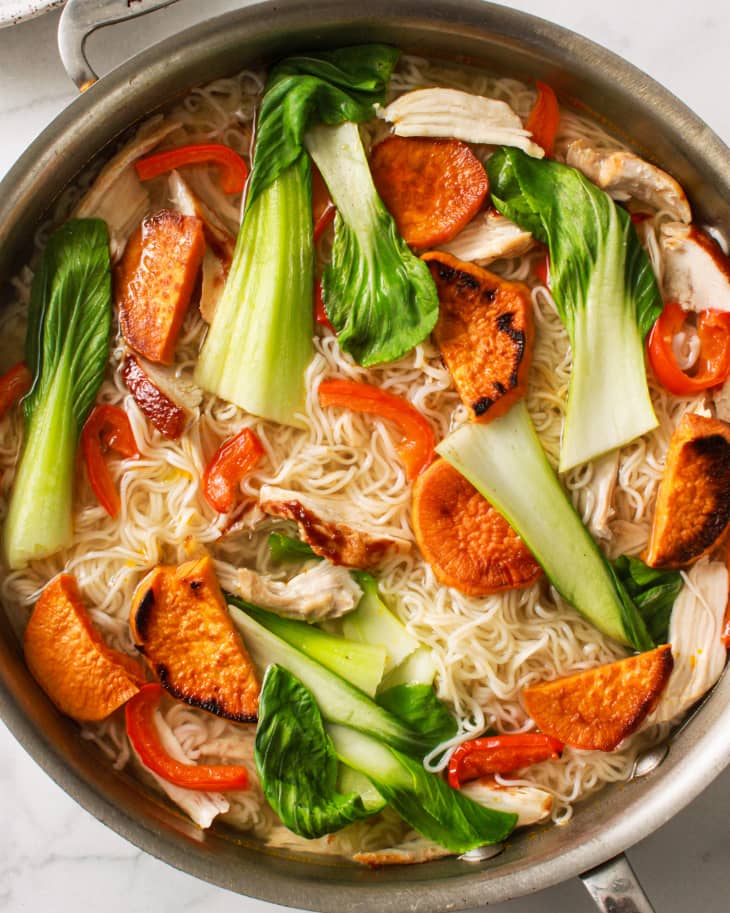 Noodles with bok choy, sweet potatoes, red bell peppers, and chicken in a pan.