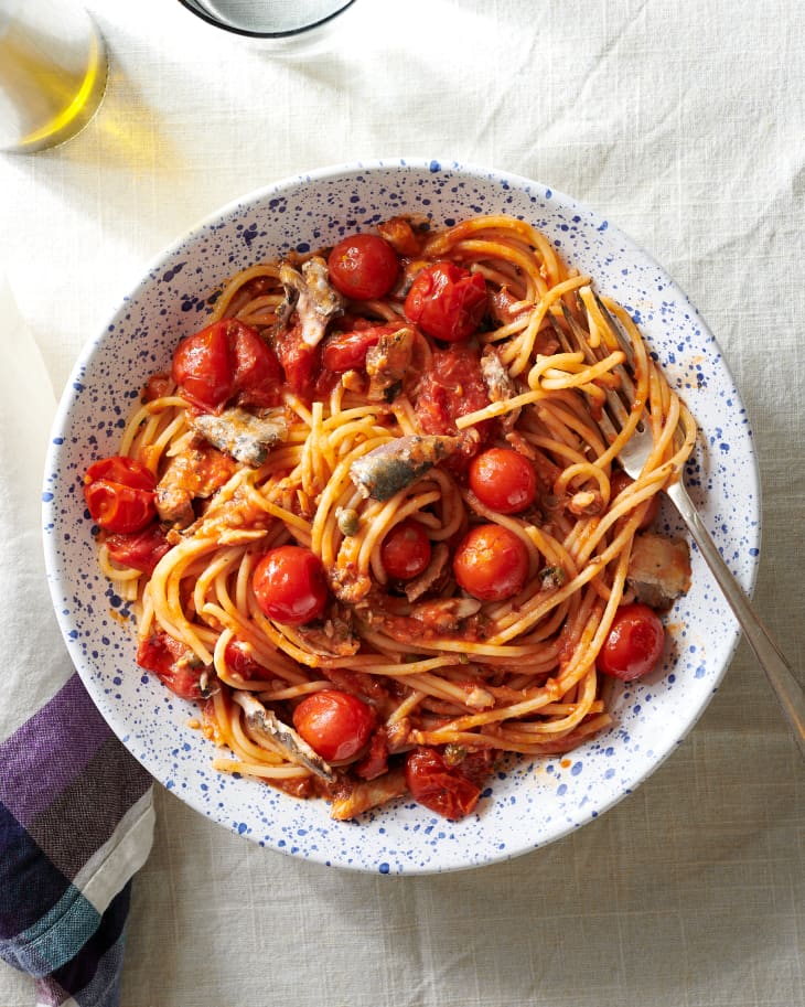 Spaghetti with sardines and cherry tomatoes in a speckled bowl on a tablecloth.