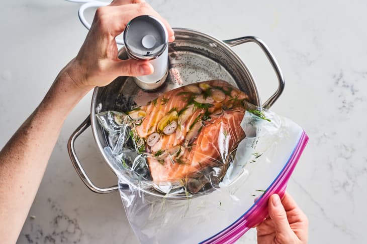 Salmon fillet with herbs and garlic in a sealed bag, submerged in a pot for sous vide cooking.