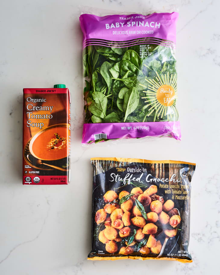 Creamy tomato soup, baby spinach, and stuffed gnocchi packages on a marble surface.