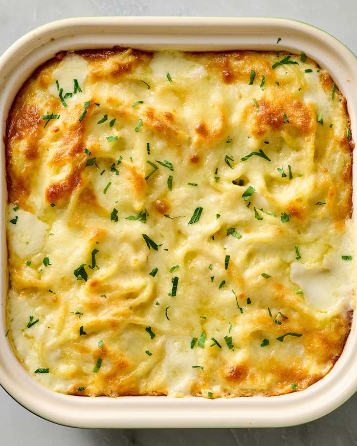 Creamy potato gratin topped with melted cheese and fresh herbs in a white baking dish.