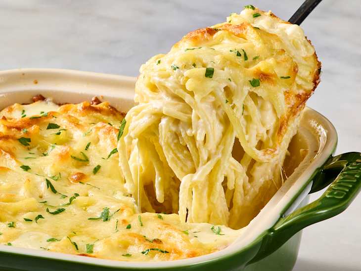 Creamy baked pasta with melted cheese and parsley, being served from a green dish.