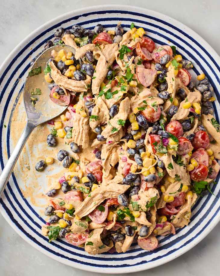 Cowboy chicken salad with shredded chicken, black beans, cherry tomatoes, corn, and fresh herbs in a striped bowl.