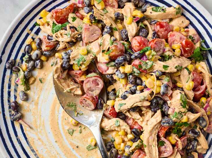 Cowboy chicken salad with shredded chicken, black beans, cherry tomatoes, corn, and fresh herbs in a striped bowl.