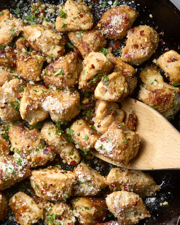 An overhead close up shot of chicken garlic parmesan bites in a cast iron skillet with a wooden spoon