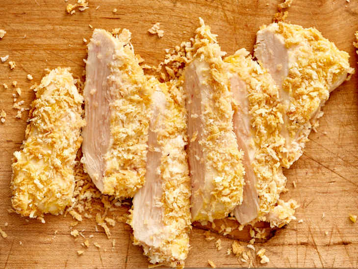 Sliced, breaded chicken tenders on a wooden cutting board, with crispy coating and visible meat.