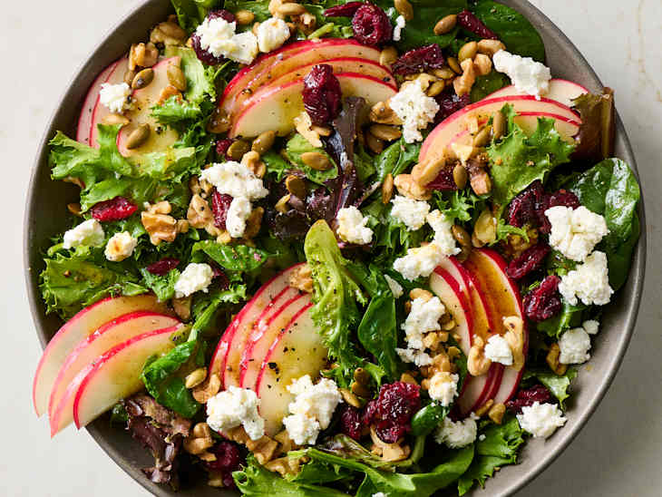 A fresh salad with mixed greens, sliced apples, goat cheese, walnuts, and pumpkin seeds.