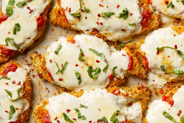 Overhead shot of baked chicken parmesan on a sheet pan, topped with red pepper flakes and basil.