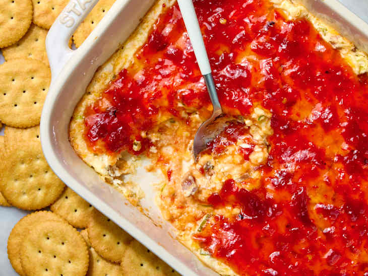 overhead shot of baked pepper jelly cream cheese in a baking dish, with ritz crackers on the surface