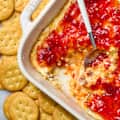 overhead shot of baked pepper jelly cream cheese in a baking dish, with ritz crackers on the surface