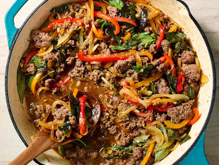 A cast iron pot filled with cooked ground beef, colorful bell peppers, onions, and leafy greens in a savory sauce.