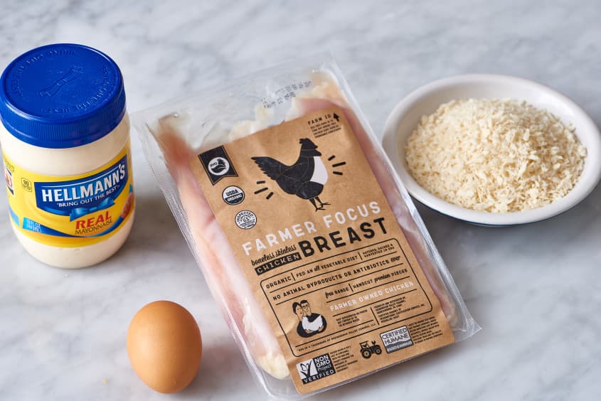 Chicken breast, mayonnaise, egg, and breadcrumbs on a marble surface for baking crispy, juicy chicken.