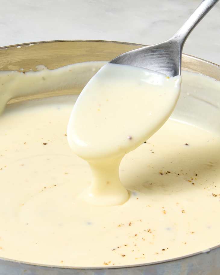 angled shot of a spoon with bechamel sauce dripping off of it