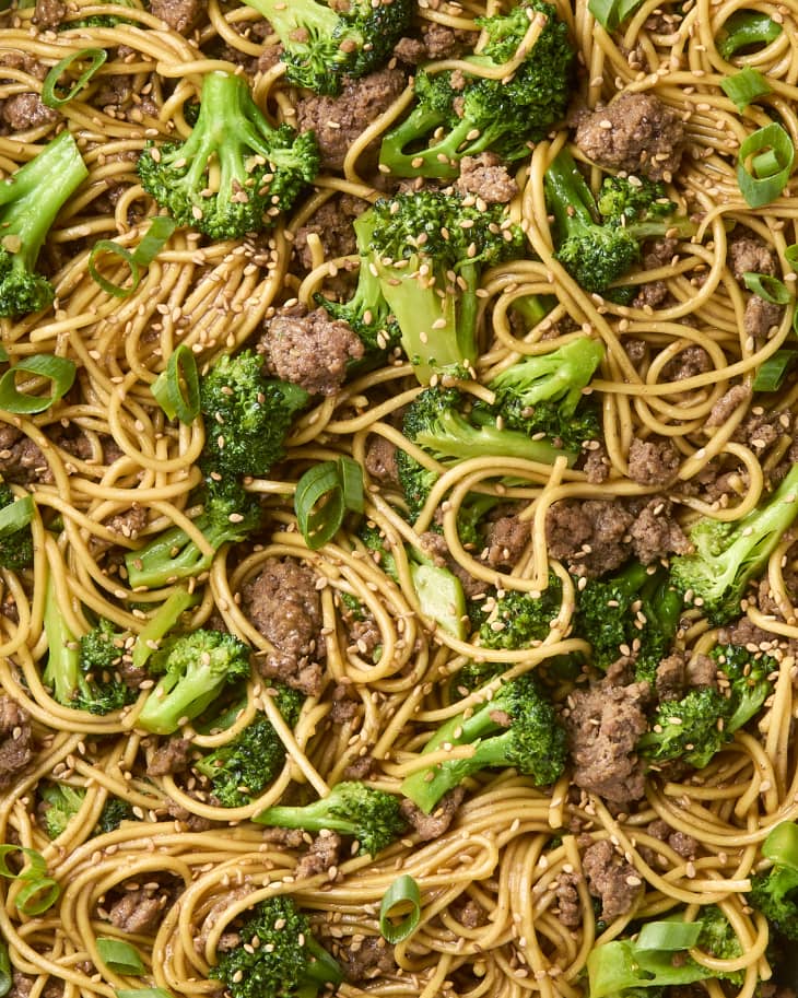 overhead shot of beef and broccoli noodles in a small white bowl, topped with sesame seeds