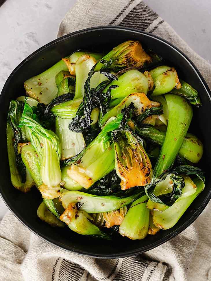 A photo of a black bowl with cooked bok choy and chopsticks on the side.