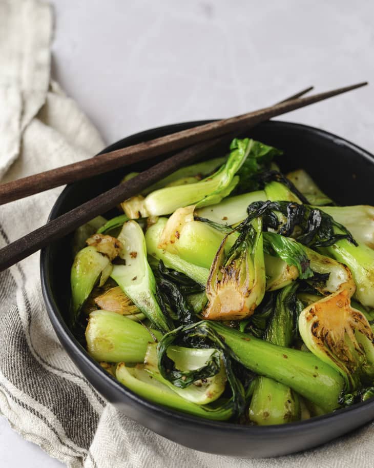 A photo of a black bowl with cooked bok choy and chopsticks on the side.