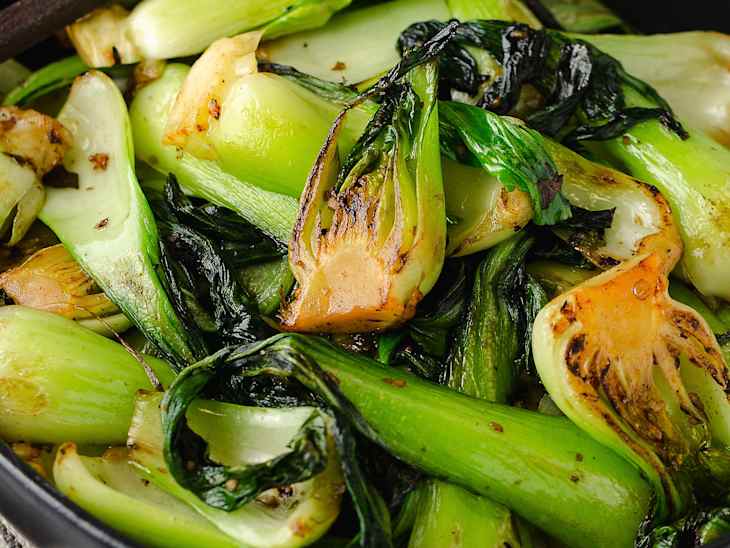 A photo of a black bowl with cooked bok choy and chopsticks on the side.