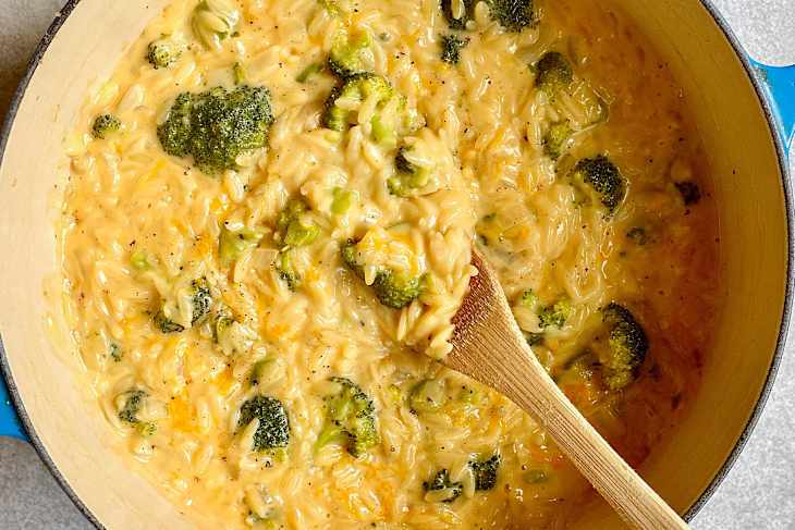 Broccoli cheddar orzo in Dutch oven with wooden spoon inside.