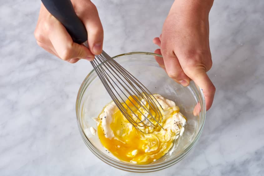 Whisking egg yolk and mayonnaise in a glass bowl for crispy chicken.