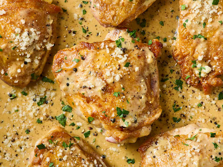 Pan-seared chicken thighs in a creamy sauce, garnished with parsley and cheese, in a stainless steel skillet.