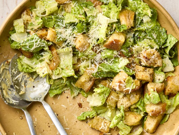 overhead shot of caesar salad in a large salad bowl, topped with parmesan cheese, with some of it missing from the bowl