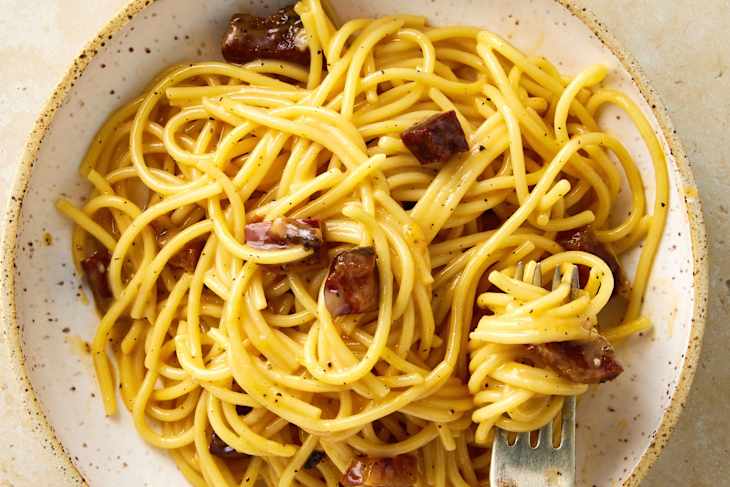 Overhead shot of carbonara  in a bowl with a fork resting in the bottom right of the bowl.