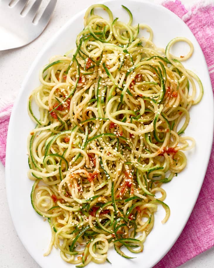 Cucumber noodles with chili-garlic sauce and sesame seeds on a white plate.