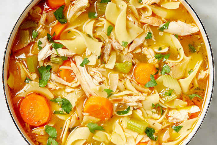 Overhead shot of chicken noodle soup in a white pot.
