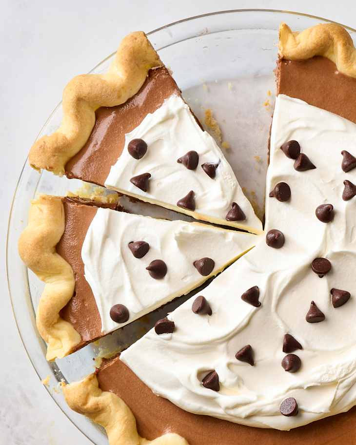 Chocolate cream pie with whipped cream topping and chocolate chips, sliced in a glass pie dish.