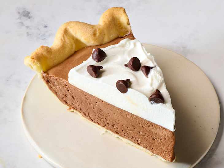 Chocolate cream pie slice with whipped cream and chocolate chips on a beige plate.
