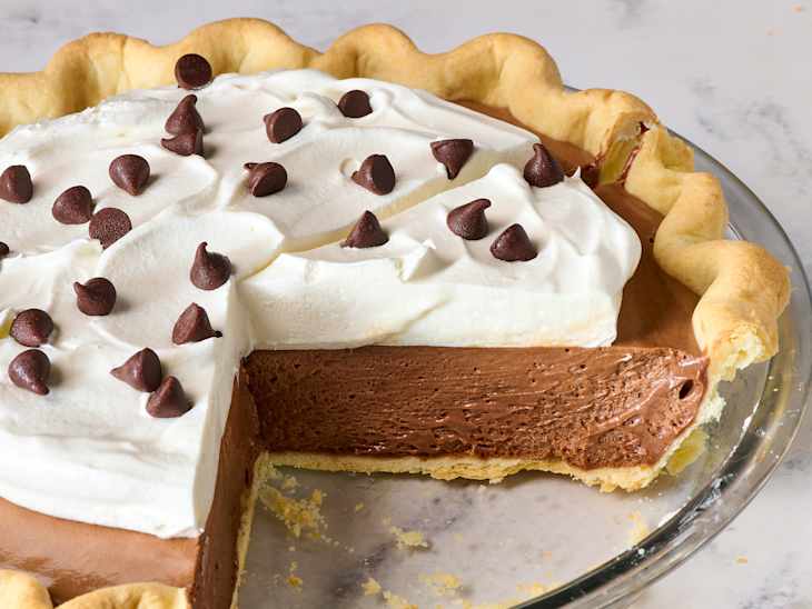 Chocolate cream pie with whipped cream topping and chocolate chips, partially sliced in a glass pie dish.