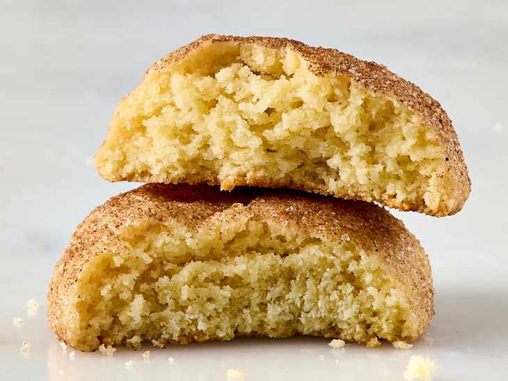 Two soft, golden-brown snickerdoodle cookies stacked, revealing a fluffy interior with a cinnamon-sugar coating.