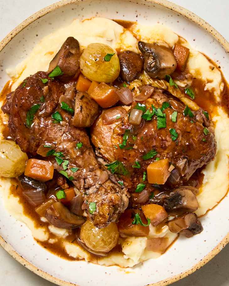 A bowl of coq au vin atop mashed potatoes.a