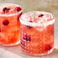 Two crystal glasses filled with a pink cocktail, garnished with ice and cranberries, rimmed with salt.