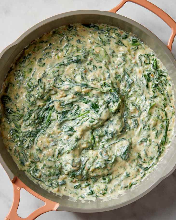 Overhead shot of creamed spinach in a light pink colored pan.