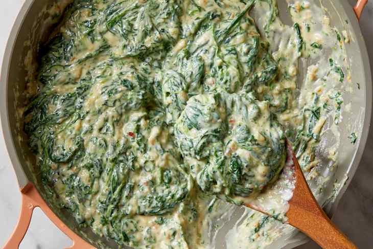 Overhead shot of creamed spinach in a light pink colored pan, with a wood spoon scooping it out.