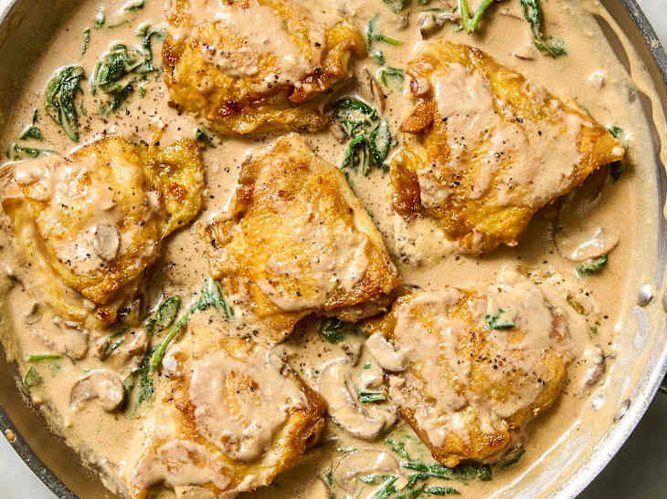 Creamy chicken thighs in a skillet with spinach and mushrooms, garnished with black pepper.
