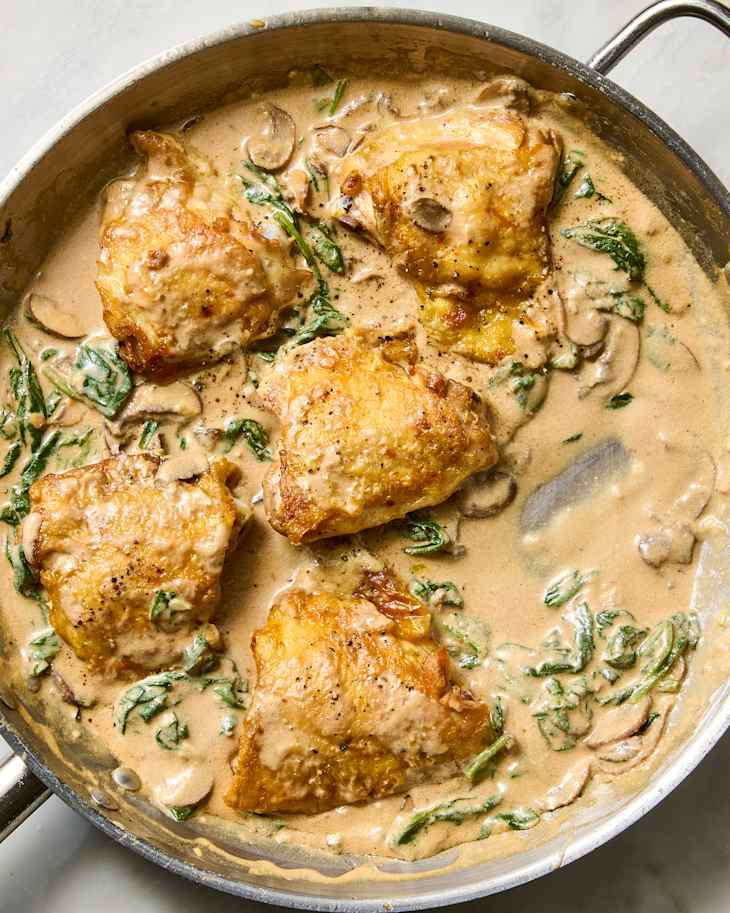 Creamy chicken thighs in a skillet with spinach and mushrooms in a rich sauce.
