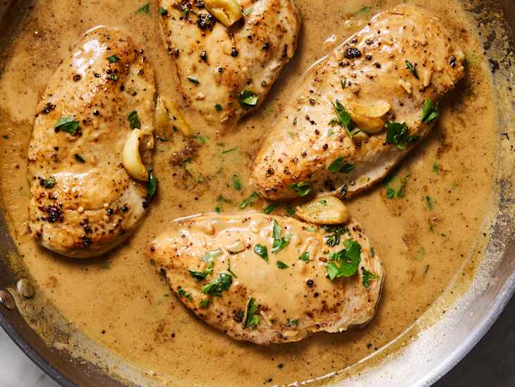 Juicy chicken breasts in a creamy sauce with garlic and parsley, cooked in a skillet.