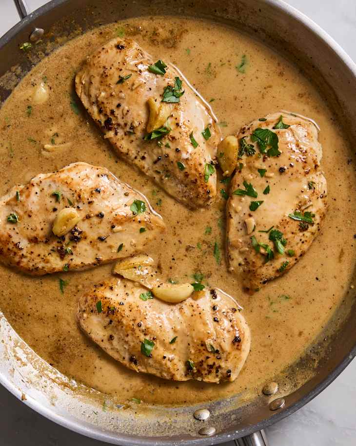 Cooked chicken breasts in a creamy sauce with garlic and parsley in a stainless steel skillet.